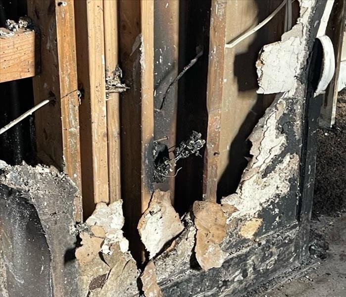 Burnt, crumbled drywall and baseboard with charred wall framing underneath