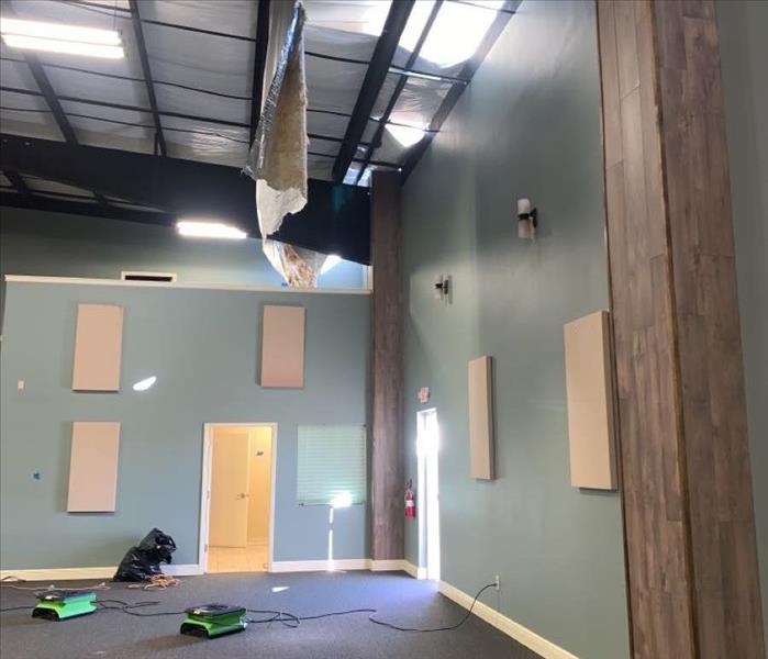 A large open carpeted area with three SERVPRO air movers pointed upward at the ceiling with a dangling sheet of insulation ha