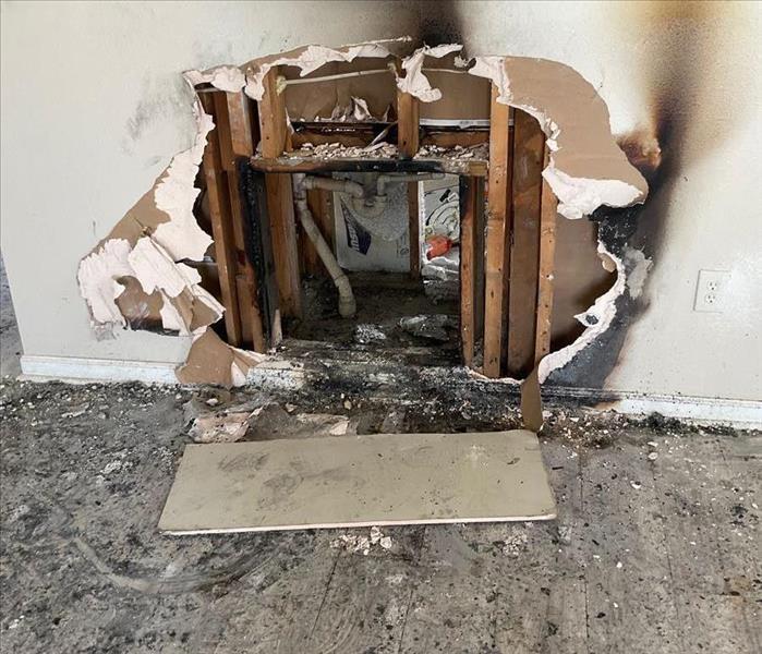 A living room wall cavity with heavy soot and smoke damage and debris on surrounding drywall and floors 