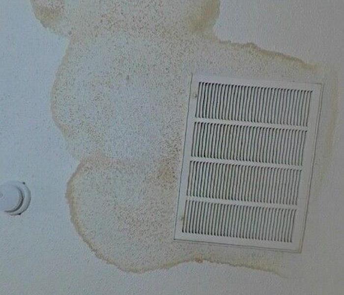 A wall with visible water stains on drywall around a vent